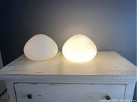 Two white frosted globe mood lights on a light colored wooden surface, neither currently illuminated, showing the shape and size of both lights side by side.