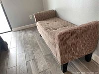 Upholstered bench with brown upholstery and white dotted pattern placed on a wooden floor next to a wall.