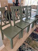 Four green wooden chairs arranged in a row inside a room, showing front and side views with visible distressed paint.