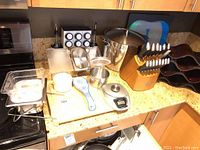 Overview of all items on kitchen countertop including cutting boards, spice jars, digital scale, sauce pot, cruet set, Chicago Cutlery knife block, and wine rack.