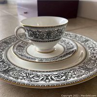Stack of dinner plate, saucer, and cup displaying decorative black floral scroll pattern and gold trim