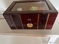 Front view of wooden humidor with glass top, showing decorative inlays and hygrometer on front.