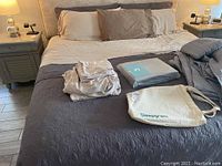 Photo of king bed showing folded sheets, boxed sheet set, pillows, comforter in gray tones on bed