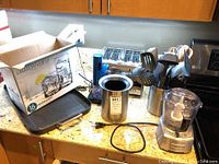 Image showing all items on countertop: 4-slice toaster, Cuisinart food chopper, wine cooler, spatulas and spoons in utensil holder, iron skillet, and boxed water glasses.