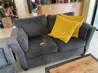Front view of gray loveseat with two yellow pillows placed on seat cushions, showing fabric texture and general condition.