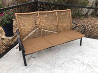 Front view of three person outdoor sofa with black metal frame and light brown woven faux wicker seat and backrest.
