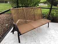 Full view of three-person outdoor sofa with brown faux wicker seating and black metal frame placed on a patio area.