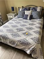 Photo showing the full bed with metal frame, headboard, bedding, and pillows in a bedroom setting.