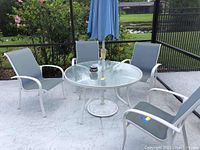 Glass top metal patio table with umbrella and four matching metal chairs with gray fabric, placed on outdoor patio