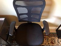 Front view of black office chair with mesh back and black fabric seat on patterned rug