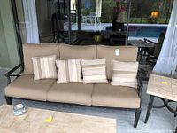 Front view of metal outdoor sofa with beige cushions and four striped pillows on patio.