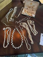 Photo showing multiple pearl necklaces, including different bead sizes and styles, laid out on table.