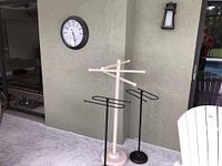 Two black metal towel racks and one white resin/plastic towel rack near a wall with outdoor clock mounted above
