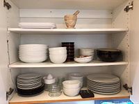 Three shelves filled with assorted plates, bowls, and mortar and pestle