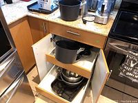 Kitchen cabinet drawers open showing Calphalon pots, mixing bowls, and pans stacked inside.
