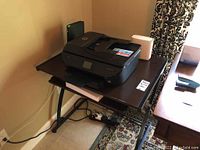 Photo showing the HP Envy Photo 7855 printer sitting on the tripod printer table with black metal legs and a pull-out tray.
