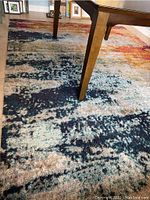 Close-up photo of the rug showing abstract multicolored blue, red, orange pattern under a wooden dining table.