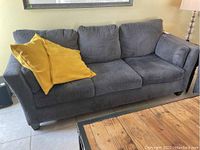 Three-quarter front view of the sofa showing the gray fabric and two yellow pillows on the left side.