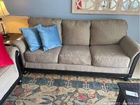 Front view of beige fabric pullout sofa with 6 cushions and 2 blue pillows on a patterned rug.