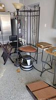 Photo showing two stools, untested floor lamp with frosted glass shade and ornate base, black metal corner shelf/coatrack with scroll work, black chair with padded seat and back, wooden luggage rack, black and white dog ramp