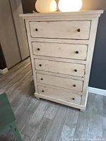 Front view of white distressed 5 drawer tall boy dresser showing scratches and black knobs.