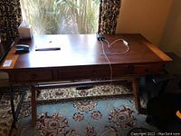 Front-facing view of entire desk showing tabletop, drawers, and tripod leg support.