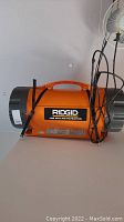 Side view of Ridgid AF21000 job site air filtration unit showing orange body, gray ends, handle on top, and attached power cord