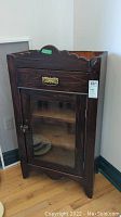 Front view of antique wooden cabinet with drawer and glass door showing brass handle and latch.