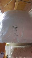 White comforter hanging wrapped in plastic with label visible indicating content as pillows and comforters.