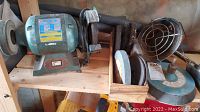 Westward bench grinder with attached grinding wheels and extra wheels in a wooden container next to a blue propane tank heater.
