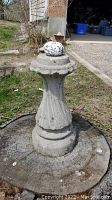 Photo of the cement pedestal base of the bird bath, showing fluted vertical design and some wear.