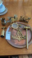 Tray with ship wheel motif, brass gavel, candleholders, napkin holder, and wine opener displayed on wood table.