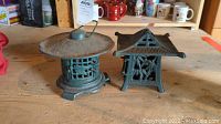 Pair of cast iron painted candle lanterns with distinct Asian-style designs sitting on wooden surface.