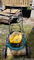 Front view of the Yard Man gas lawn mower showing handlebar, yellow motor cover, and green metal base with wheels.