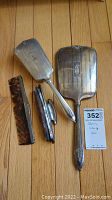 Four-piece sterling silver vanity set with two hand mirrors, hairbrush, and comb on wooden floor.
