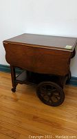 Wooden tea wagon with dropleaf sides, shown folded with large wooden spoked wheels.