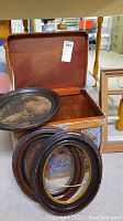 Two oval wood frames with vintage art prints, basket with lid opened showing woven inside, and two rectangular wood frames leaning on each other.
