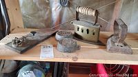 Vintage flat irons, Morse code telegraph key, and cast iron weights arranged on a wooden shelf, showing condition and layout of the lot.