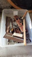 Bin filled with assorted vintage hand tools including wooden levels, hand scrapers, and metal measuring tools.
