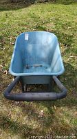 Front view inside the blue plastic wheelbarrow showing the tub and handles on grass.