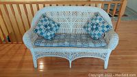 White wicker love seat with blue and white checkered seat cushion and two side pillows.