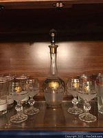Bohemian glass decanter and six matching frosted gold floral goblets on shelf