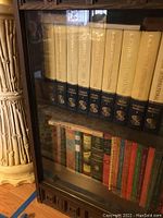 Photo of shelves behind glass case showing a set of Encyclopedia International volumes with cream and navy blue spines, labeled with volume numbers and titles.