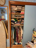 Wide view of closet showing shelves with folded linens and stacks of women's clothing below hanging on rod