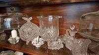 Cut glass candy dish with lid, crystal ice bucket, candle holders, small decorative floral piece, oil decanter, creamer pitcher on shelf