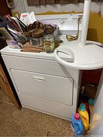 View of white Kenmore 600 dryer with various items placed on top including shoes, jars, and small containers. Dryer appears solid and intact with front drop-down door.