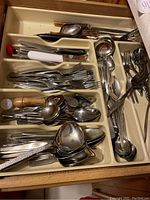 Silver-tone flatware including forks, spoons, knives in a kitchen drawer organizer.