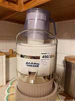 Front view of the Jack LaLanne power juicer showing the white body with chrome band and purple plastic pusher on top, label with brand and model visible.