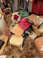 Pile of assorted towels and some bedding items on carpet with packaged blanket and footstool