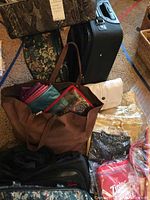 Photo showing brown tote bag with colorful pouches, white purse, several new purses in clear packaging, floral suitcase, and portion of black suitcase.
